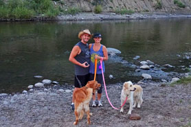 Couple with their dogs standing in front of private pond at Pagosa Riverside Campground and Camper Cabins in Pagosa Springs, Colorado.