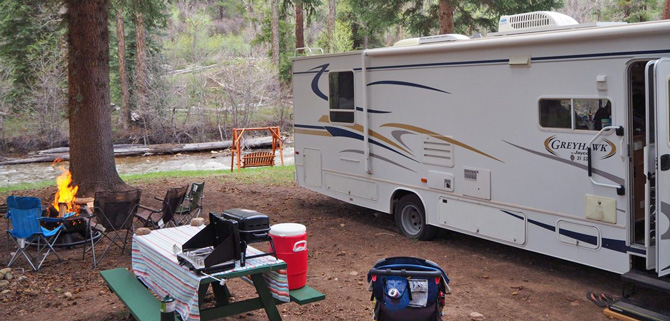 Large wooded RV Site with fire pit, picnic bench and bench swing next to stream at Stoner RV Resort and Tent Campground in Dolores, Colorado