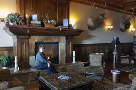 Woman sitting on stone hearth next to fireplace in the Trophy Parlor room at Antlers Inn near North Park in Walden, Colorado