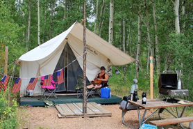 Camper relaxing at a glamping tent site with elevated wood floors and picnic table at Aspen Acres Campground located within the Greenhorn Valley in Rye, Colorado.