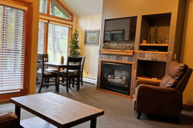 Inside view of Great Room with gas fireplace, rocking char, flat screen tv, and table with chairs at Aspen Winds on Fall River Vacation Suites in Estes Park, Colorado.