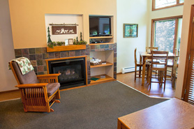 Inside view of Great Room with gas fireplace, rocking char, flat screen tv, and table with chairs at Aspen Winds on Fall River Vacation Suites in Estes Park, Colorado