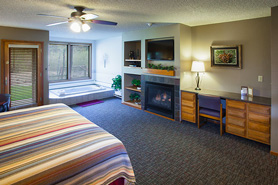 Inside view of the spa suite with in-room spa tub, gas fireplace, flat screen tv, door to patio, and built in desk at Aspen Winds on Fall River Vacation Suites in Estes Park, Colorado