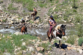 Horseback riders on trail crossing stream with Avalanche Outfitters at Redstone Stables in Redstone, Colorado.
