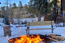 Relaxing campfire area with sitting bench behind cabins along riverside path at Blackhawk Cabins in Estes Park, Colorado.