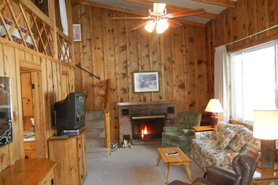 View of living area inside log cabin with tv, loft and fireplace at Blackhawk Cabins in Estes Park, Colorado.