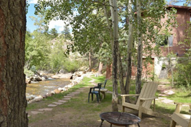 Relaxing shaded sitting area behind cabins along riverside path at Blackhawk Cabins in Estes Park, Colorado.