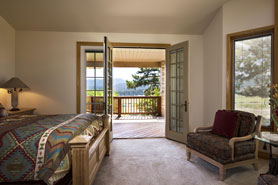 Mountain view out the french doors to a covered deck inside a bedroom of the View House at Cabins on the Ranch in Cotopaxi, Colorado.