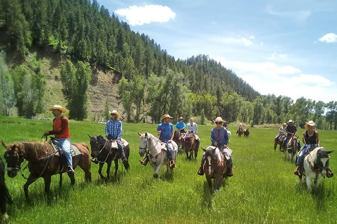 Group of horseback riders on a day ride with Colorado Trails Ranch in a lush green meadow near Durango, CO