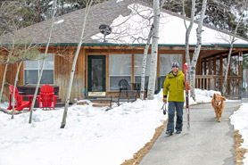Man carrying skis with his dog walking down path in front of Stonehouse Cabin at Creekside Chalets and Cabins Vacation Rentals in Salida, Colorado.