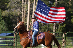 Cowgirl on horseback carrying a large US Flag celebrating the 4th of July at High Country Stampede Rodeo in Winter Park, Colorado.