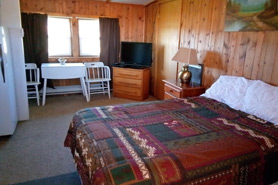 Interior view of cabin with queen bed, flat screen hdtv, cozy table and chairs, and kitchette at Hill Top General Store, Cabins and Antiques in Red Feather Lakes, Colorado.