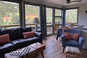 View of living room with couch, dining table and chairs with huge picture windows and an outdoor deck at Green Mountain Falls Vacation Rentals in Green Mountain Falls, Colorado.