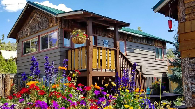 View of cabins with garden in bloom, picnic table and bird feeder at Lupin Village in Grand Lake, Colorado.