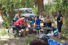 Family eating at shaded park bench with person in wheelchair at West Creek Picnic Area in the Naturita-Nucla Area, Colorado