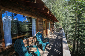 View of a large secluded shaded deck in the trees with comfortable chairs and bbq grill at one of the log cabin rentals at Oleo Ranch in Lake City, Colorado.