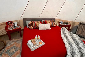 Inside view of 23-foot galmping tent with queen bed, wood-stove, bed side dressers and a welcome tray at Peaceful Peaks Ranch in Boncarbo, Colorado near Trinidad.