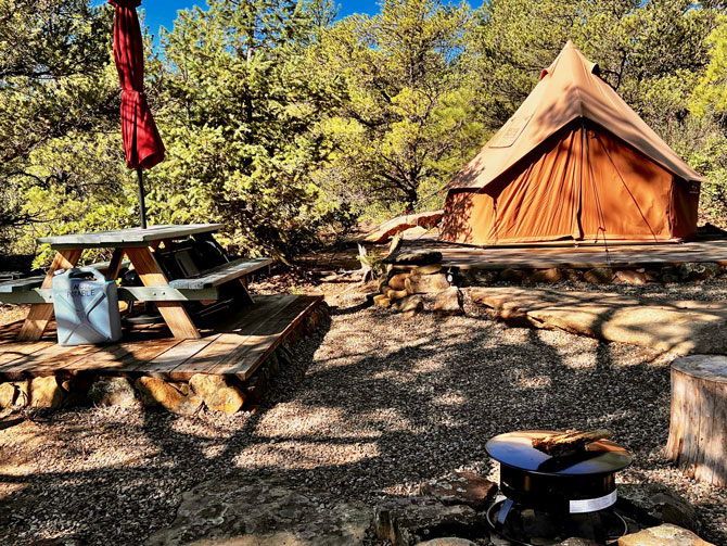 Outside view of raised 10-foot glamping tent with picnic bench and fire pit at Peaceful Peaks Ranch in Boncarbo, Colorado near Trinidad.