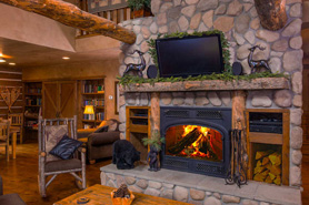 Living room area inside log cabin rental with stone fireplace, flat screen tv, and comfortable chairs at Pinebrook Vacation Rentals in Estes Park, Colorado.