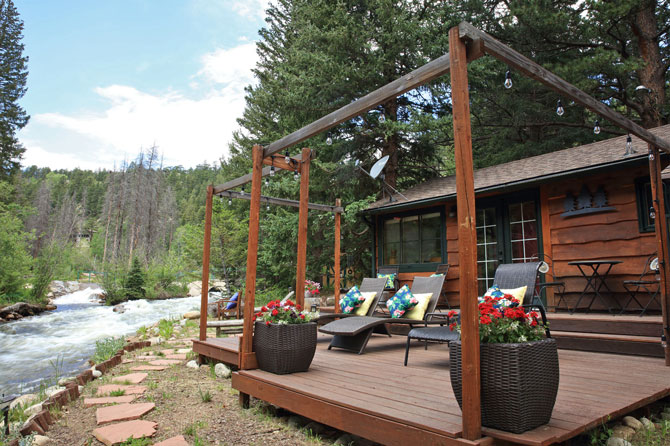 Riverfront view from back deck of cabin furnished with comfortable chaise lounge chairs at River Bend Mountain Retreat in Allenspark, Colorado.