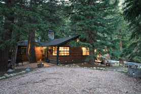 Cozy cabin in the trees with stone front porch, table, and chairs lit up at night at River Bend Mountain Retreat near Estes Park and Lyons, Colorado.