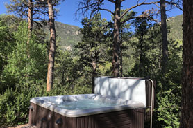 Private outdoor hot tub shaded by trees at Pikes Peak Guest Cabin at Rocky Mountain Lodge in Cascade, Colorado.