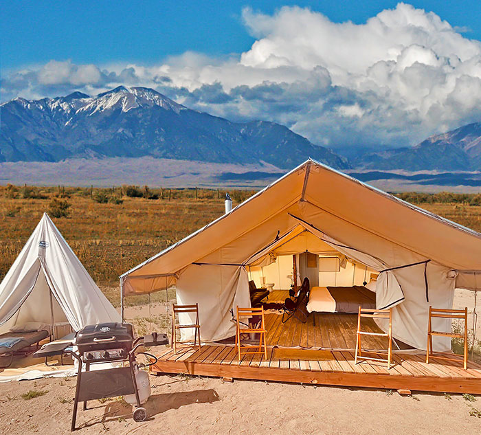 View of Deluxe Canvas Galmping Tent including a raised wood platform floor, queen size bed and couch with mountain view and Great Sand Dunes National Park in the distance at Rustic Rook Resort located in Alamosa, Colorado.