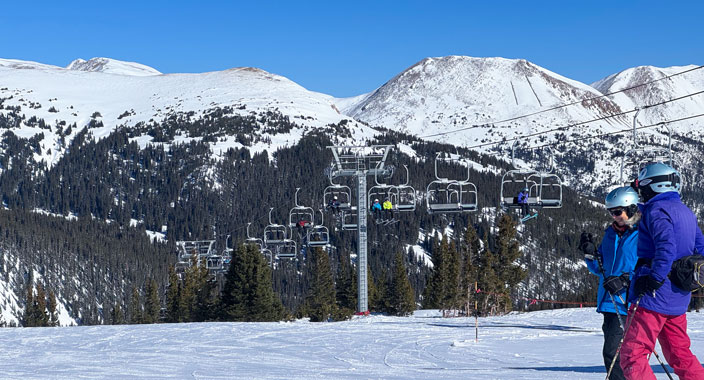 View of skiers with ski lift and snow capped mountains in the background at a Colorado Ski Resort.