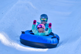 Adult with child laughing while tubing together down a lane at Echo Mountain Ski Resort in Idaho Springs, Colorado.