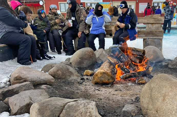 Families getting warm eating snacks and drinking hot beverages around a large fire-pit at Colorado Adventure Park near Winter Park in Fraser, Colorado