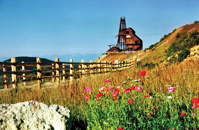 A fence beside a bed of flowers, leading up to an abandoned mine. Come visit the City of Mines in Victor, Colorado. See this view from the Trail of Gold hiking trails.