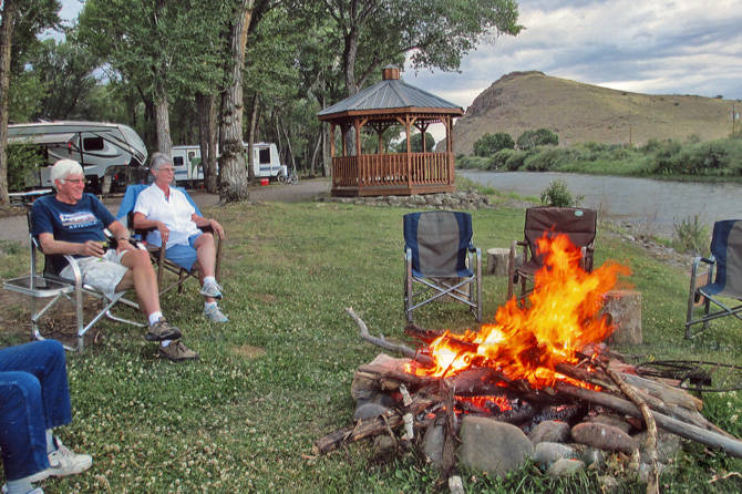 Family sitting around campfire along the Rio Grande River with gazebo and RV's in background at Woods and River RV Park and Campground in Del Norte, Colorado.